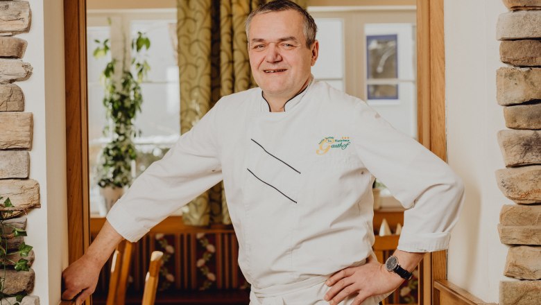 Wirt Gerhard Perthold, © Niederösterreich Werbung/Klaus Engelmayer Ein Mann in weißer Kochuniform steht lächelnd in einem Restaurant.