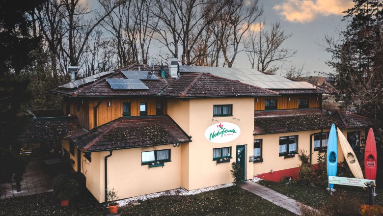 Naturfreunde Bootshaus, © Niederösterreich Werbung/ David Schreiber Ein Gebäude mit Solarpanelen auf dem Dach und einem Schild mit der Aufschrift 'Naturfreunde'. Vor dem Gebäude stehen drei bunte Kanus.