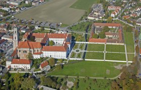 Luftaufnahme eines gro&szlig;en Geb&auml;udekomplexes mit roten D&auml;chern und Gartenanlagen.