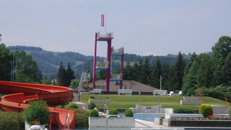 Ein Freibad mit Rutsche, Sprungturm und gr&uuml;ner Umgebung.