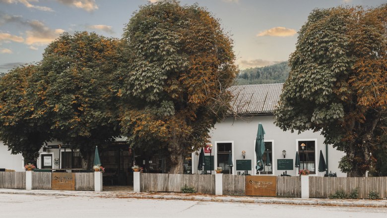 Ein traditionelles Wirtshaus in Lilienfeld mit großen Bäumen und einem Holzzaun davor.