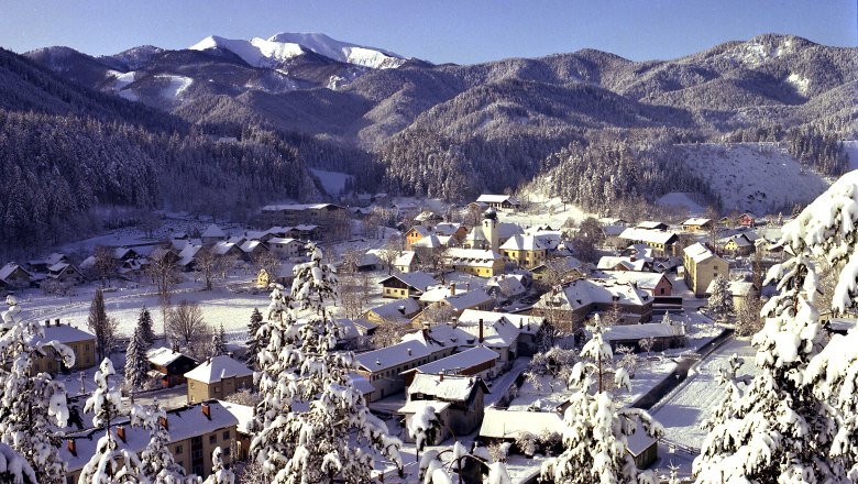 Winterliche Landschaft von St. Aegyd mit schneebedeckten Häusern und Bergen im Hintergrund.