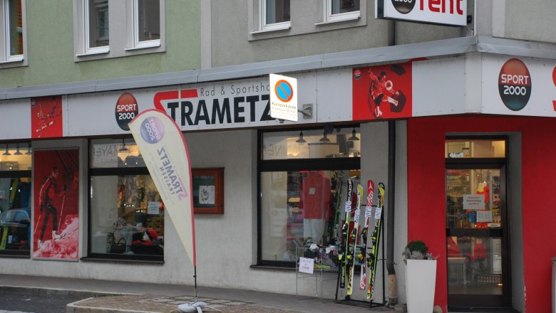 Au&szlig;enansicht eines Sportgesch&auml;fts namens Strametz mit Skiern und Sportbekleidung im Schaufenster.