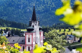 Basilika Mariazell vor bewaldeten H&uuml;geln, umgeben von gr&uuml;ner Landschaft.