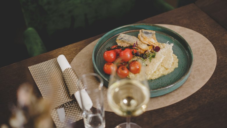 Ein Teller mit gegrilltem Goldbrassenfilet, Zitronenrisotto und Kirschtomaten, serviert auf einem Holztisch mit einem Glas Weißwein.