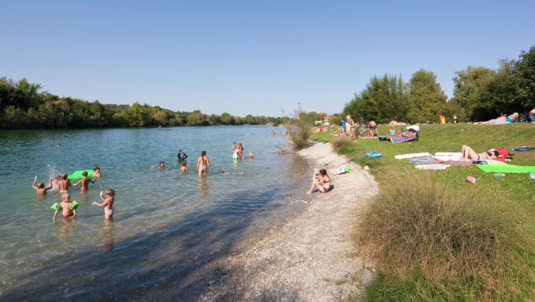 Menschen schwimmen und entspannen am Ratzersdorfer See an einem sonnigen Tag.