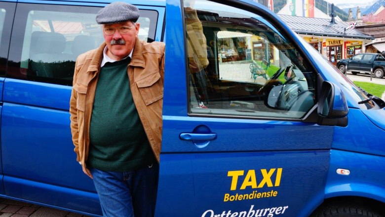 Ein Mann steht neben einem blauen Taxi mit der Aufschrift 'Taxi Botendienste Orttenburger'.