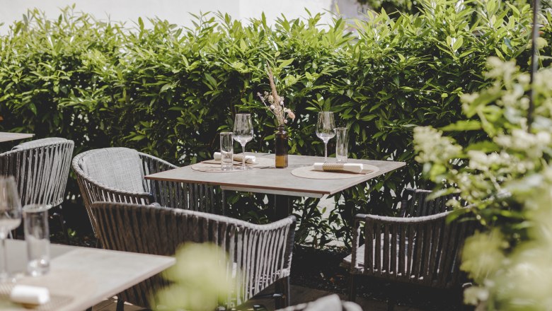 Ein gemütlicher Gastgarten mit gedeckten Tischen und grüner Hecke im Hintergrund.