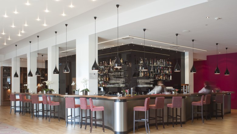 Moderne Hotelbar mit roten Stühlen und schwarzen Hängelampen.