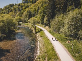 Zwei Radfahrerinnen fahren entlang des Radwegs neben einem Fluss.