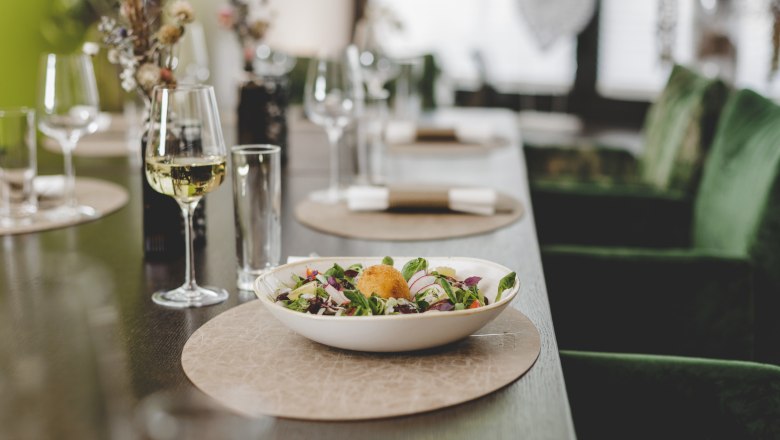 Ein gedeckter Tisch mit einem Salatteller und einem Glas Weißwein.